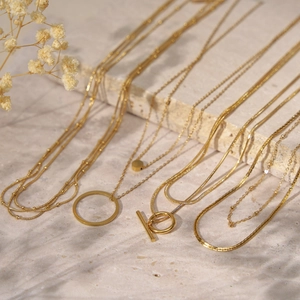 Elegant multi-layered 18K gold plated necklaces on stone with soft shadows