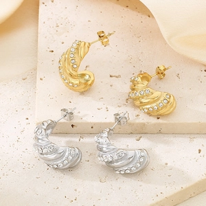 Detail of spiral C-shaped gold and silver earrings with sparkling white crystals