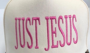 Detailed close-up of pink 'JUST JESUS' embroidery on a beige twill baseball cap