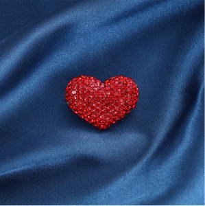 Detailed macro view of red heart rhinestone brooch on luxurious dark blue silk background