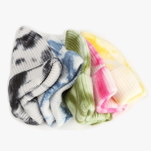 Flat lay of colorful tie-dye knit beanies in blue, pink, and yellow textured wool