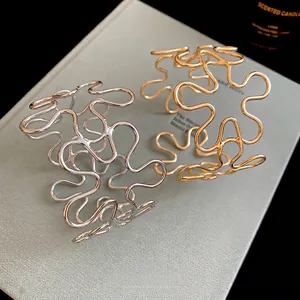 Artistic hollow metallic open cuff bracelets in gold and silver finishes on a textured book