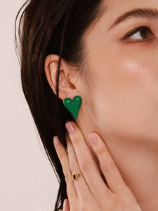 Close-up of vibrant green enamel heart earring on model with polished gold finish detail