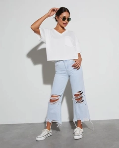 Dettaglio di jeans a gamba larga strappati azzurri con t-shirt bianca con scollo a V