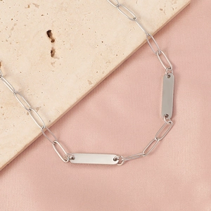 Macro shot of silver rectangular bar pendant on paperclip chain necklace over silk