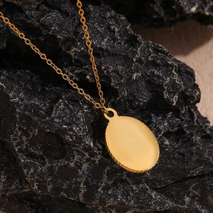 Detail of 18K gold plated oval sun pendant necklace on a dark textured rock background