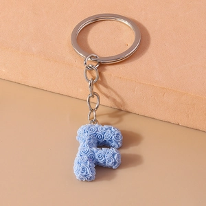 Detail of light blue letter F keychain with embossed rose pattern and silver metal ring
