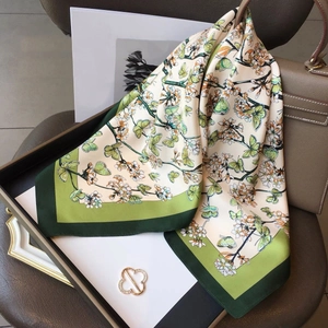 Elegant silk scarf with green floral butterfly pattern styled on a luxury leather handbag