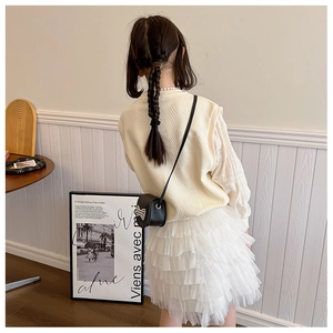 Detail of girls beige knit vest and white tutu skirt with a black bow pearl handbag