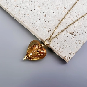 Close-up of heart-shaped amber pendant with gold foil texture and golden chain