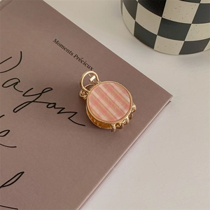 Detailed close-up of a small golden metal hair claw clip with pink striped resin panel