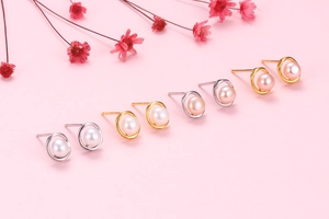 Macro shot of silver and gold pearl earrings on a pink background with dried flowers