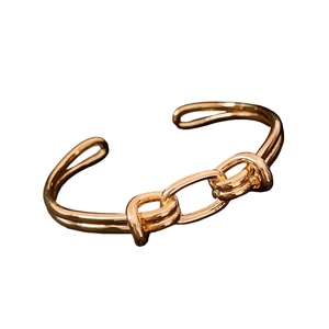 Bracciale rigido ovale aperto placcato oro 18 carati con design a nodo e catena su sfondo bianco