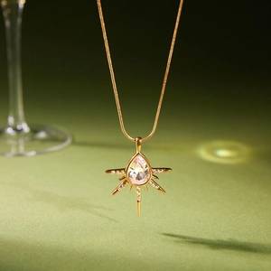 Collier doré avec pendentif cristal goutte étoilé sur fond vert émeraude texturé