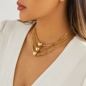 Close-up of a layered gold chain necklace featuring polished metal beads on a model