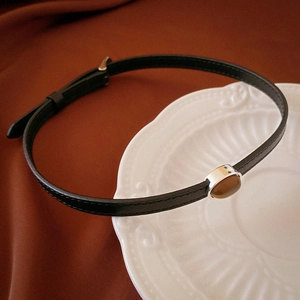 Detail view of tiger eye stone pendant on black leather choker necklace against a white plate