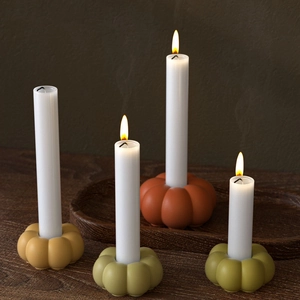 Close-up of matte pumpkin candle holders in autumn colors with lit long white candles