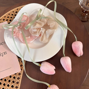 Detailed view of pink and beige tulip scrunchies with green ribbons in a decorative dish