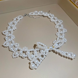 Detailed view of the handcrafted pearl bow necklace with golden beads on a jewelry tray
