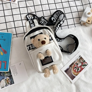 Detail of white canvas chest bag with 3D plush bear and stylish lettered strap