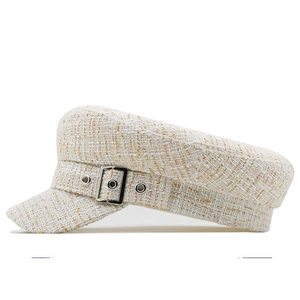Detail of tweed sailor cap featuring white and gold woven texture with silver buckle