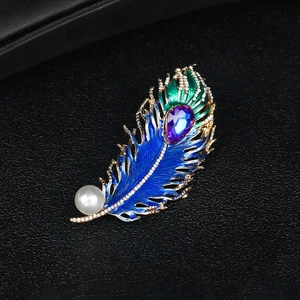 Vintage peacock feather brooch with colorful enamel, crystals, and a pearl drop on black background