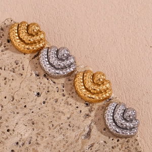 Macro detail of hammered gold and silver fan-shaped earrings on a textured stone base