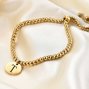 Detailed view of 18K gold beaded bracelet with an engraved T-letter round pendant