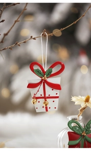 Close-up of a festive gift box Christmas ornament with red bow and gold bells on a tree