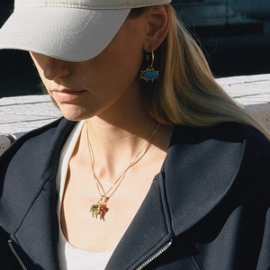 Close-up of golden evil eye earrings and multi-charm necklace on a model