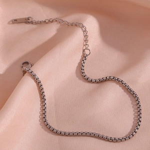 Macro shot of silver stainless steel box chain with lobster clasp on silk fabric