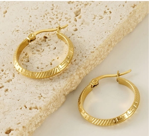 Detail of gold Greek key pattern round hoop earrings on a textured stone surface
