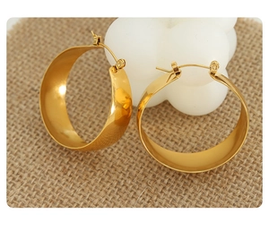 Macro detail of polished 18K gold plated thick U-shape hoop earrings on woven texture