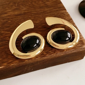 Detail of vintage gold spiral earrings featuring a large black oval gemstone on wood