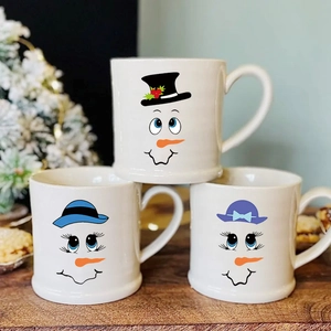 Three snowman ceramic mugs with festive cartoon expressions on a cozy wooden table