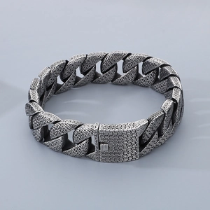 Detail of silver Cuban chain bracelet with intricate woven texture and square snap clasp