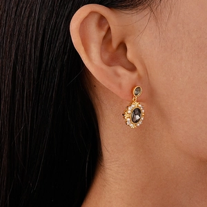 Close-up of vintage gold drop earring with grey oval stone and pearl accents on model