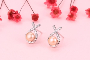 Close-up of pink freshwater pearl earrings with silver cross design and zircon details