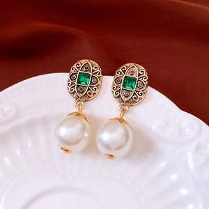 Detail of vintage gold earrings with emerald green stones and white pearl drops