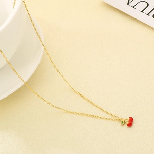 Detail of gold cherry pendant necklace with red enamel fruit and green leaf accents