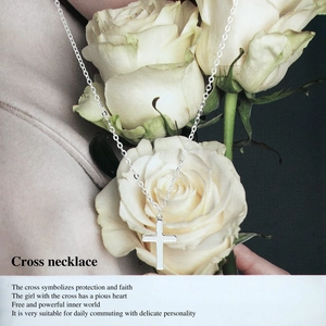 Close-up of polished silver cross pendant on O-chain against white roses backdrop