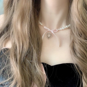 Detailed close-up of pearl necklace with pink silk bow and hollow heart cross pendant