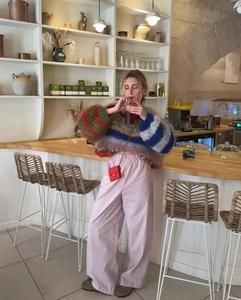 Detail of colorful striped knitted sweater and pink wide-leg pants in a cafe setting