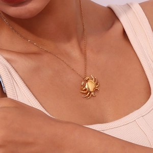 Close-up of a crab-shaped 18K gold plated pendant necklace worn by a model