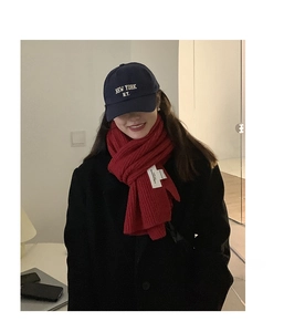 Close-up of deep red chunky knit wool scarf with a white brand label and navy cotton cap