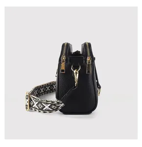 Detail view of black lychee texture crossbody bag with double zippers and woven strap