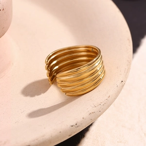 Détail d'une bague multicouche en acier doré 18 carats sur un plateau en céramique beige