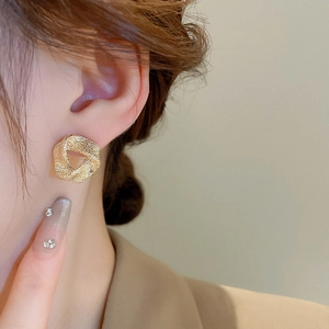 Macro shot of gold geometric earrings with fine hammered texture worn by a model