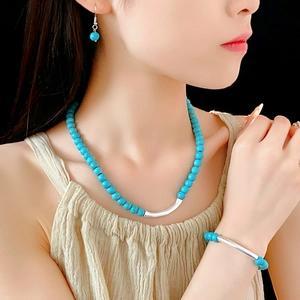 Détail d'une parure de bijoux en turquoise avec tubes argentés portée sur mannequin