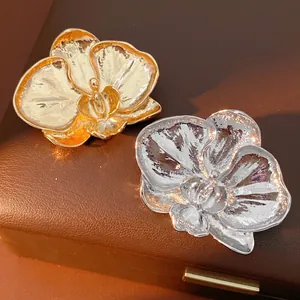 Elegant metal orchid brooches in gold and silver set on textured leather box lid
